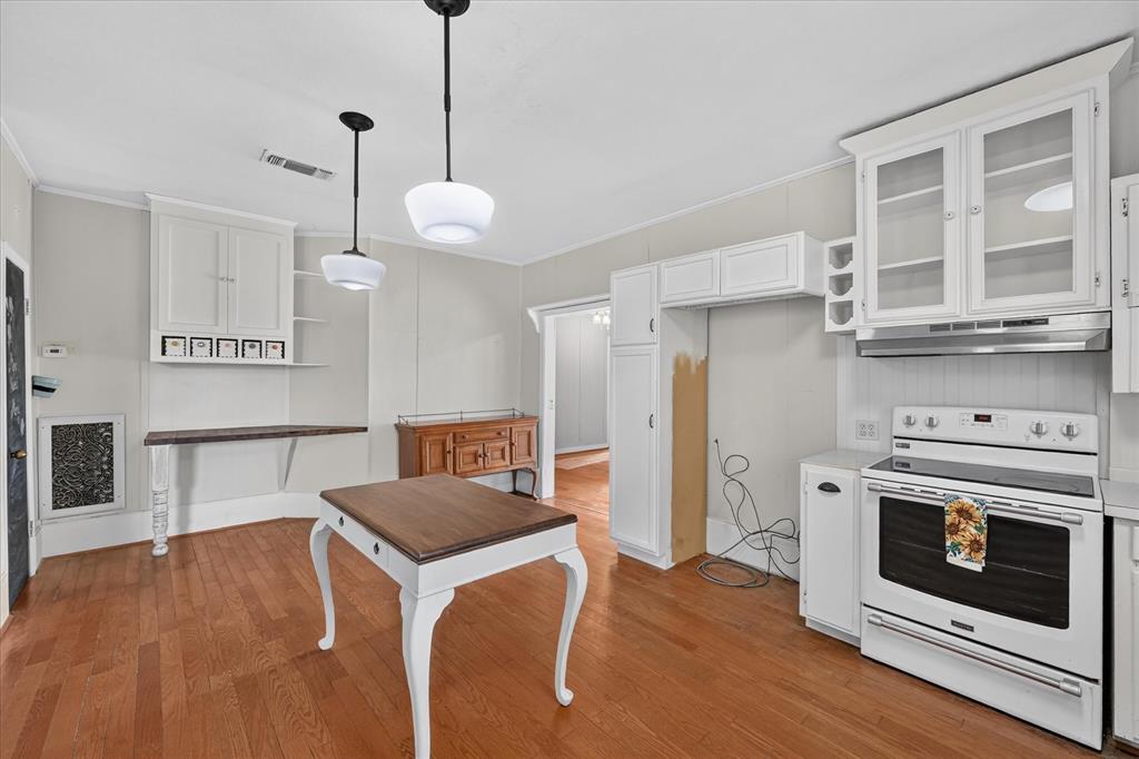 304 East Main Street Itasca, TX 76055 - Photo 14 of 38 Hardwood-finish flooring, white cabinetry with glass inserts, built-in shelving, pendant lighting, and a white electric range