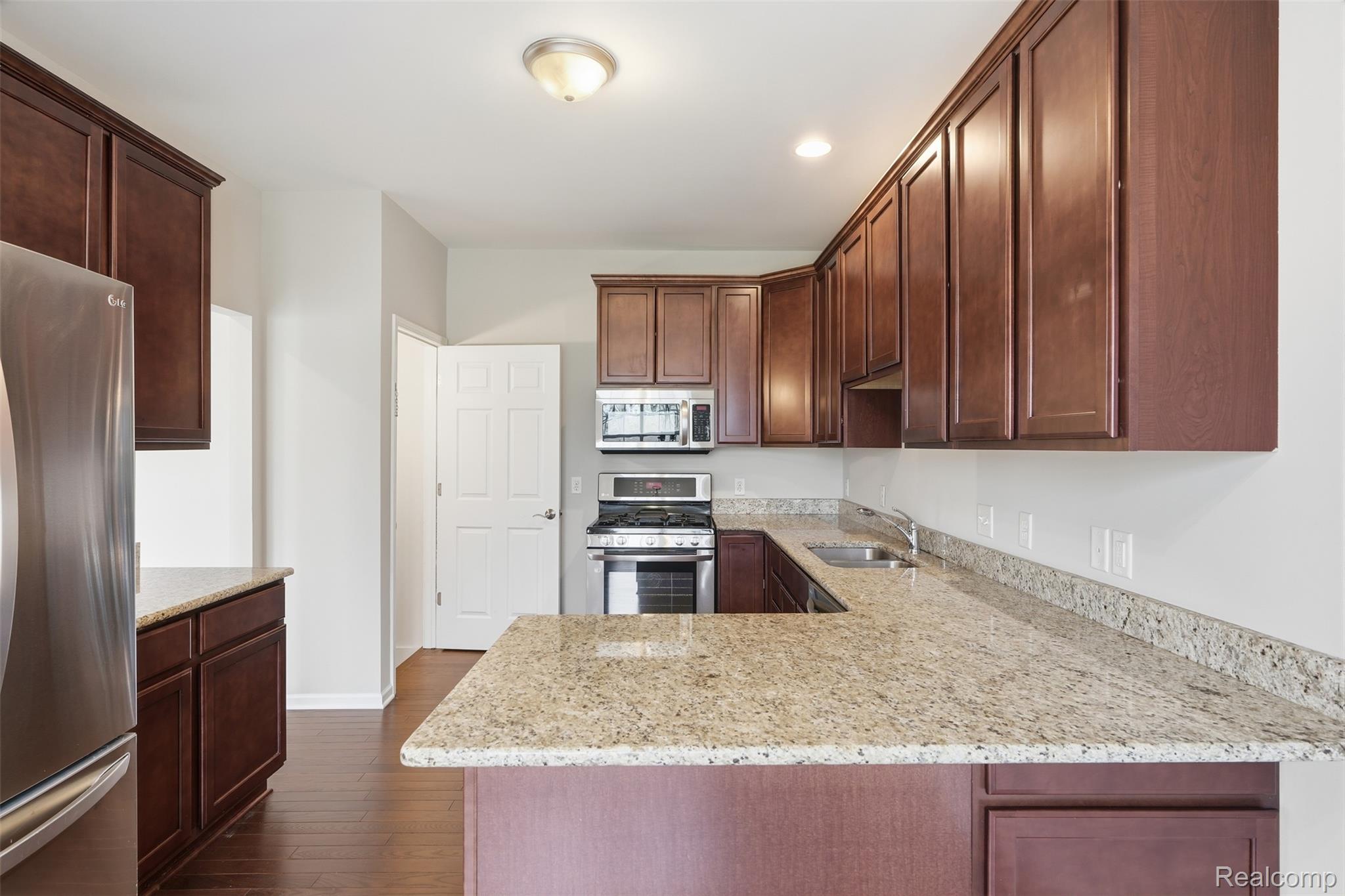 41594 Mitchell Road Novi, MI 48377 - Photo 11 of 35 Kitchen with light stone countertops, stainless steel appliances, dark wood-style flooring, dark wood finish cabinets, and a peninsula