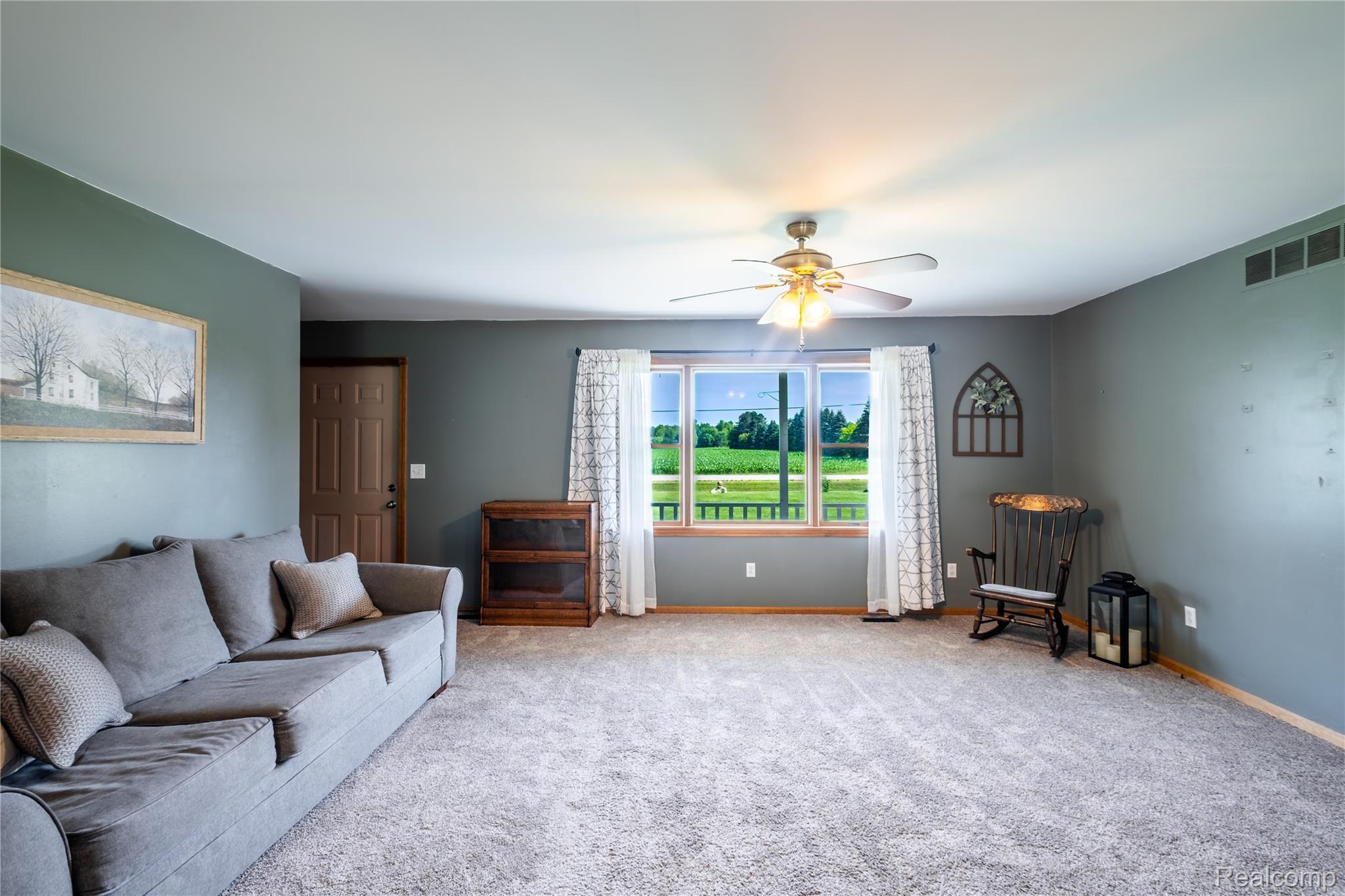 9600 Hamill Road Otisville, MI 48463 - Photo 7 of 32 Carpeted living area featuring a large window with white curtains, a ceiling fan with light fixture, and a paneled entry door