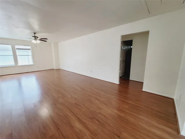 a view of an empty room with wooden floor and a ceiling fan