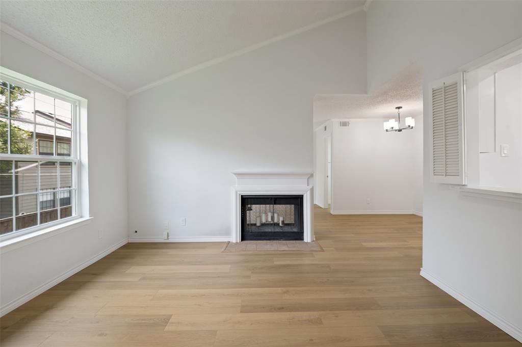 5300 Keller Springs Road, Unit 2042 Dallas, TX 75248 - Photo 9 of 28 Vaulted ceiling living area featuring wood-finish flooring, a white mantel fireplace with a dark tile hearth, and a multi-pane window