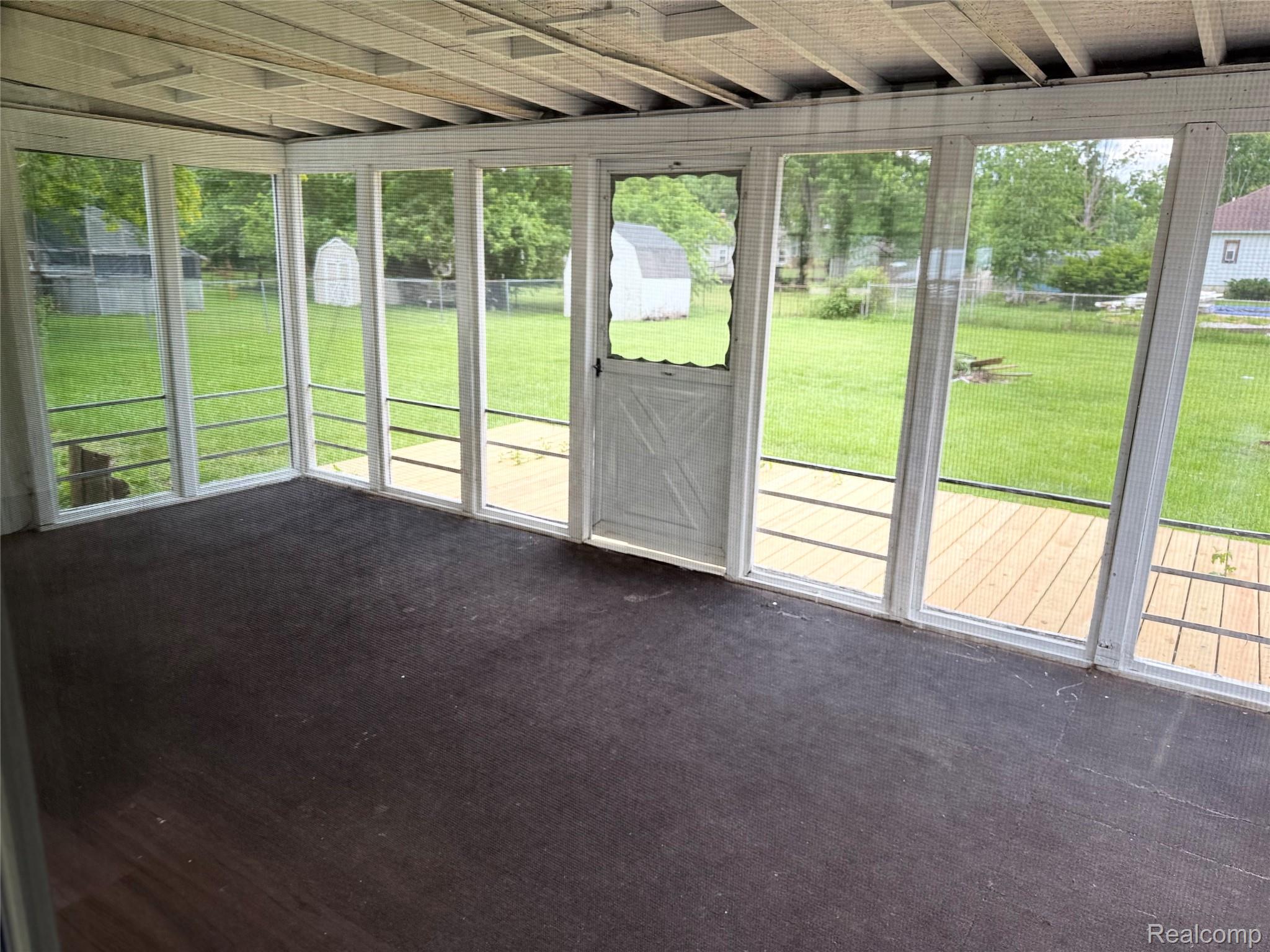 5347 Mapletree Drive Flint, MI 48532 - Photo 7 of 10 Screened porch featuring a full-light exterior door with crossbuck detail, dark flooring, and exposed ceiling joists