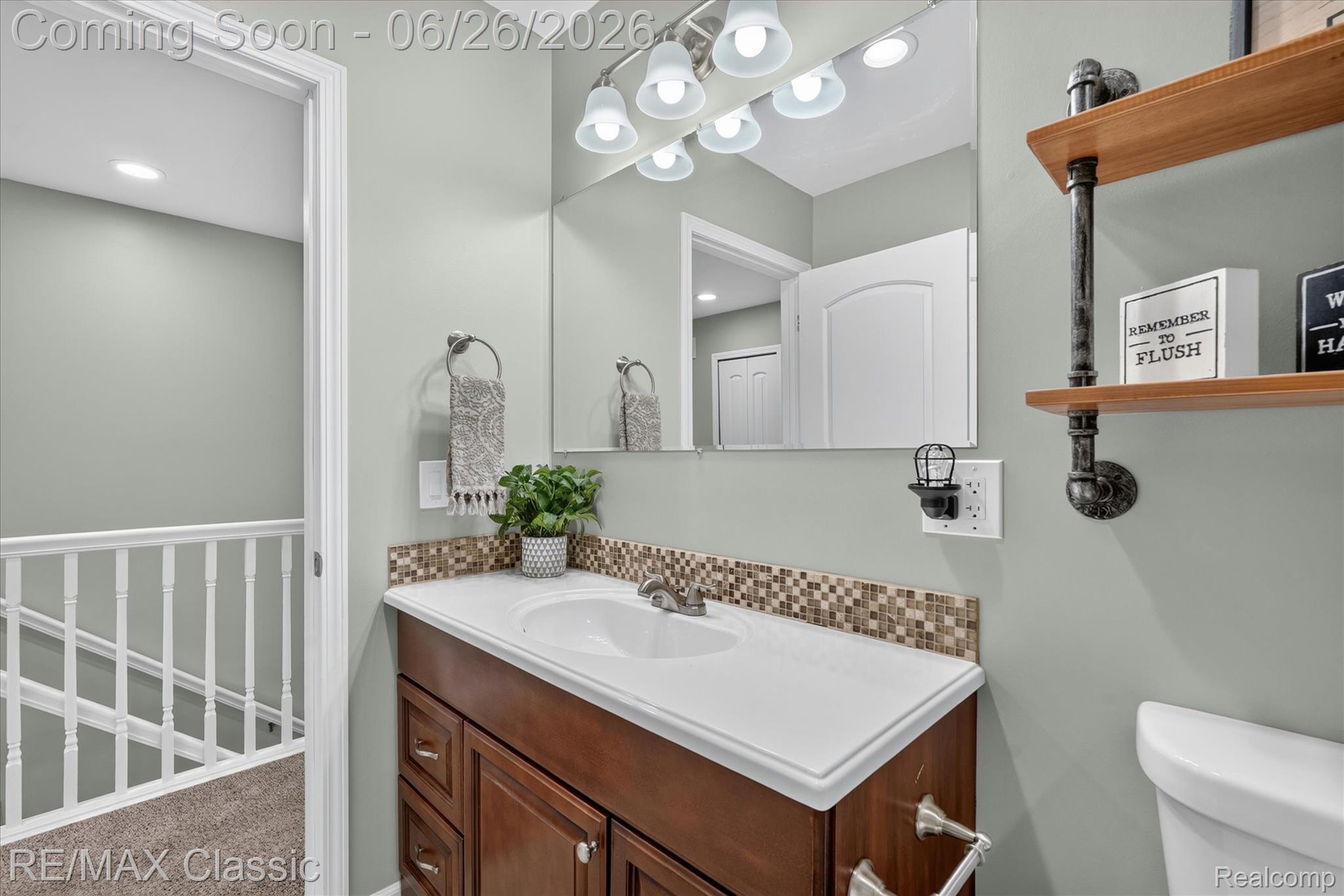 3205 North Milford Road Highland, MI 48357 - Photo 26 of 53 Bathroom vanity featuring a white countertop, mosaic tile backsplash, dark wood-finish cabinetry, and a large wall mirror with integrated lighting