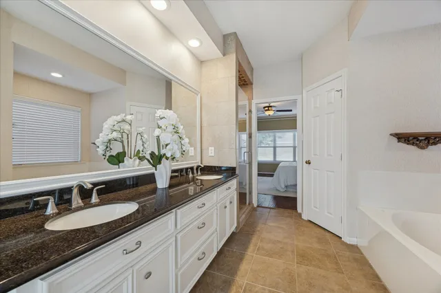 a spacious bathroom with a granite countertop double vanity sink a mirror and a bathtub