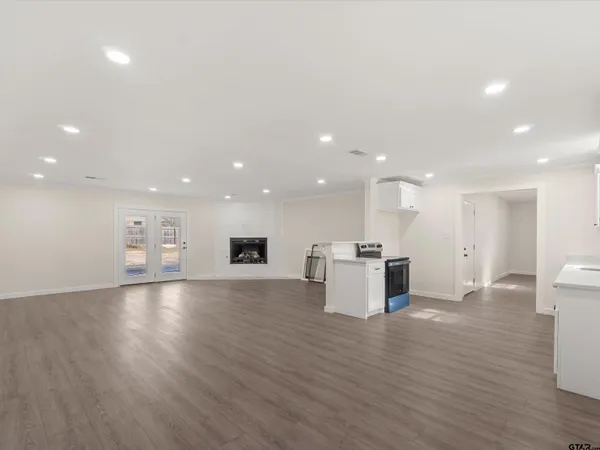 a view of an empty room with wooden floor and kitchen