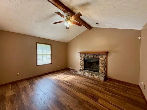 a view of an empty room with wooden floor fireplace and a window