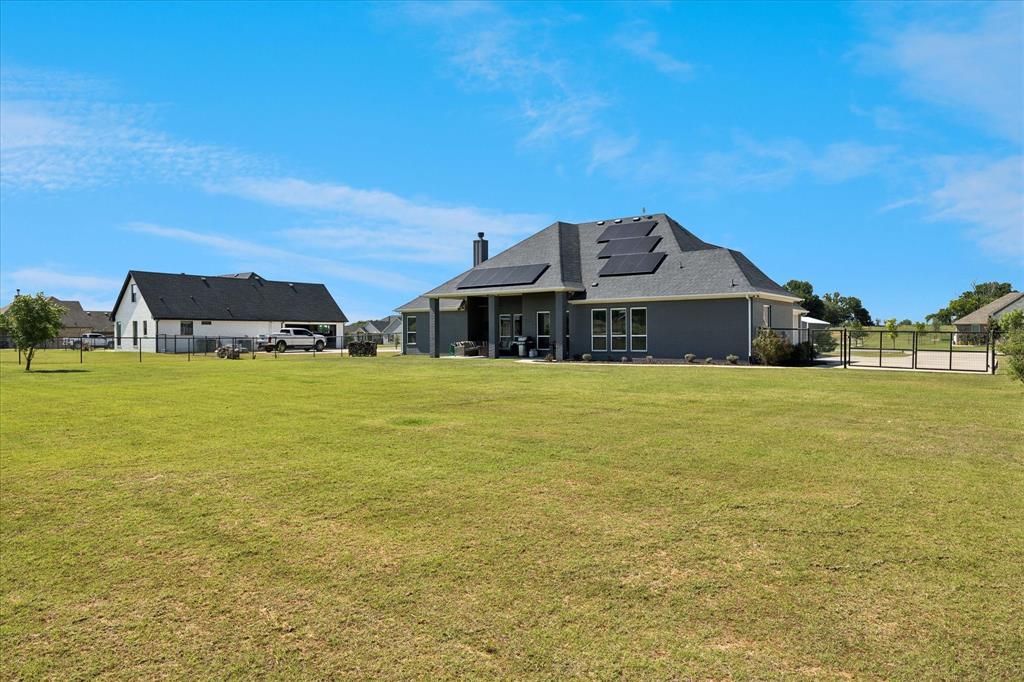 112 Friendship Way Boyd, TX 76023 - Photo 25 of 29 Expansive green lawn surrounds the property, featuring a gray-toned home with multiple windows, a covered patio, and a fenced-off paved area
