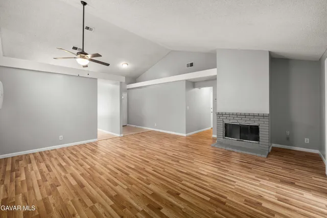 a view of an empty room with wooden floor fireplace and a window