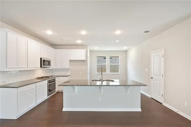 a kitchen with stainless steel appliances granite countertop a stove a sink and a refrigerator with white cabinets