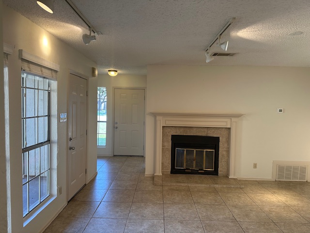 331 Fantail Loop, Unit B Austin, TX 78734 - Photo 5 of 16 Unfurnished living room with rail lighting, light tile patterned floors, a tiled fireplace, and a textured ceiling
