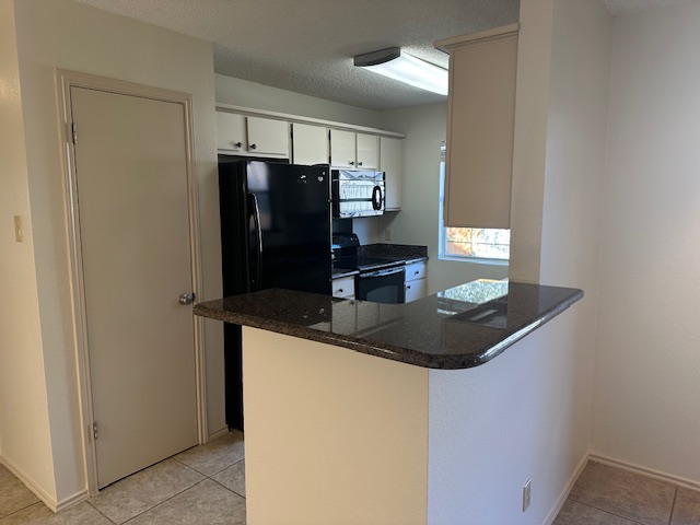 331 Fantail Loop, Unit B Austin, TX 78734 - Photo 9 of 16 Kitchen with a peninsula, black appliances, a textured ceiling, white cabinetry, and dark stone counters