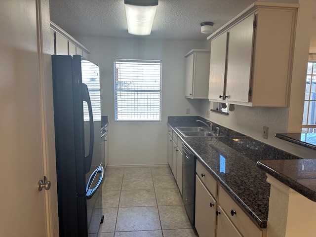 331 Fantail Loop, Unit B Austin, TX 78734 - Photo 10 of 16 Kitchen with freestanding refrigerator, a textured ceiling, dark stone counters, light tile patterned floors, and dishwasher