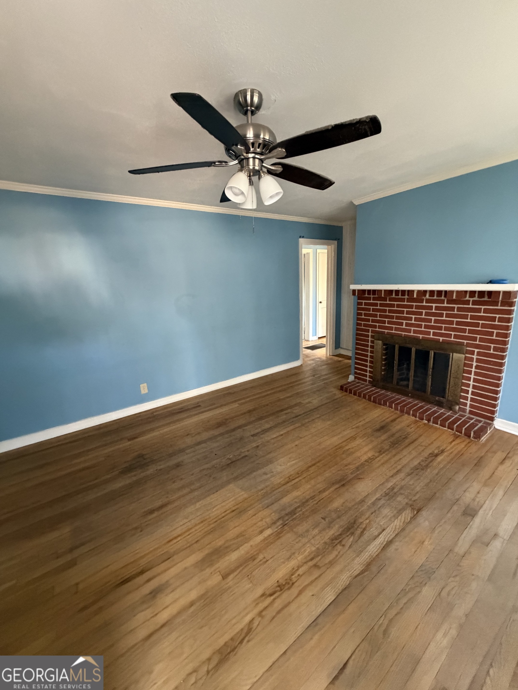 2006 Stonewall Street Dublin, GA 31021 - Photo 5 of 12 an empty room with wooden floor a ceiling fan and a fireplace