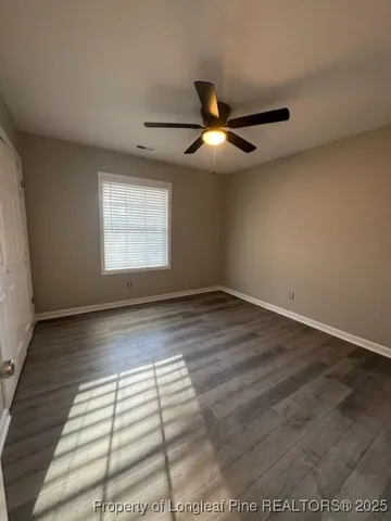 an empty room with wooden floor fan and windows
