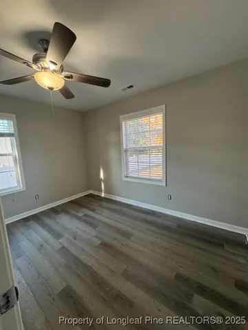 an empty room with wooden floor fan and windows