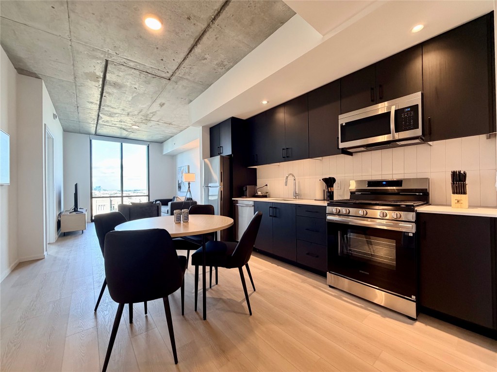 5501 La Branch Street, Unit 2108 Houston, TX 77004 - Photo 4 of 12 a kitchen with stainless steel appliances kitchen island granite countertop a stove a sink dishwasher a dining table and chairs with wooden floor