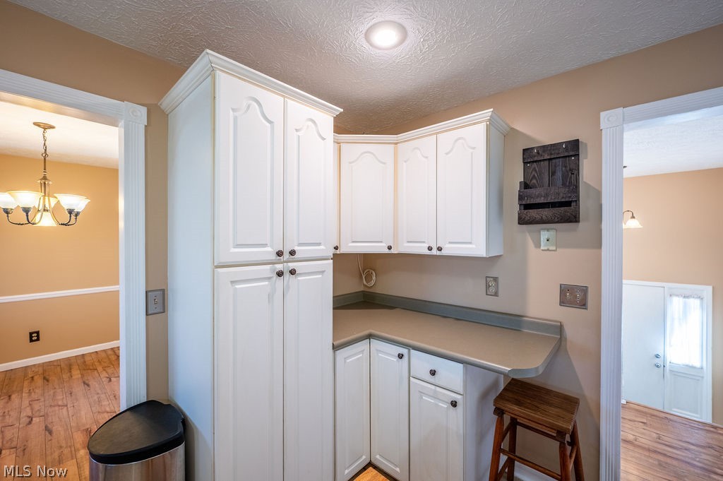 3601 River Road Vienna, WV 26105 - Photo 10 of 40 Kitchen featuring white cabinets, light wood-style flooring, a breakfast bar area, a chandelier, and a textured ceiling