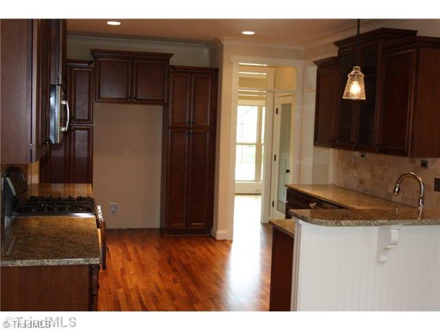 8902 West Pepper Court Oak Ridge, NC 27310 - Photo 4 of 16 Kitchen. The Kitchen has richly stained cabinetry and granite countertops. Pantry cabinets encase the refrigerator opening, and there is a separate pantry accessed by a glass door.