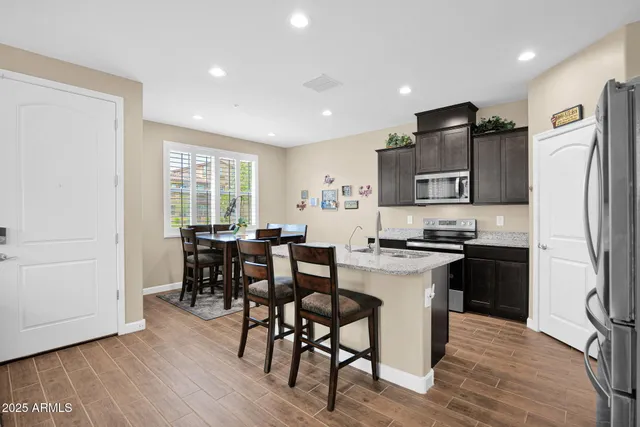 a kitchen with stainless steel appliances granite countertop a stove a refrigerator a sink a dining table and chairs with wooden floor