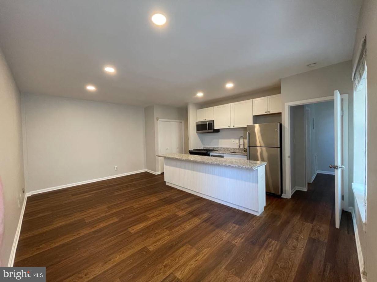 1669 Columbia Road Northwest, Unit 215 Washington, DC 20009 - Photo 22 of 28 a large kitchen with a center island wooden floor stainless steel appliances and a window