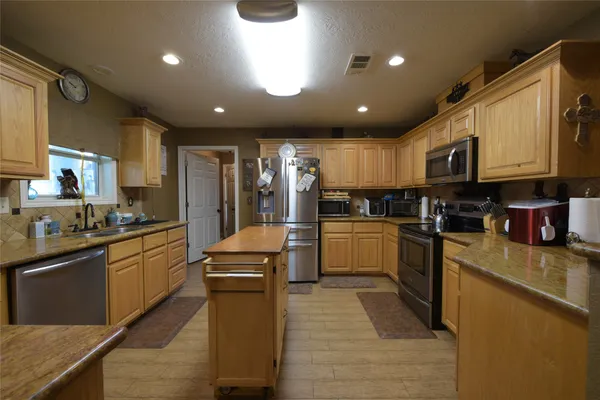 a kitchen with stainless steel appliances granite countertop wooden cabinets a sink a stove a oven a dining table and chairs