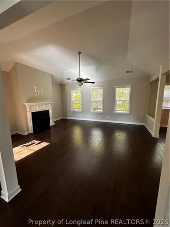 an empty room with wooden floor fireplace and windows