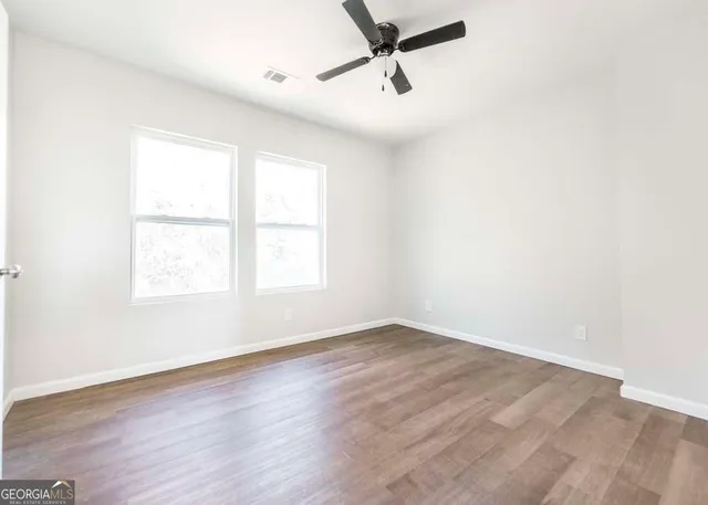 an empty room with wooden floor fan and windows