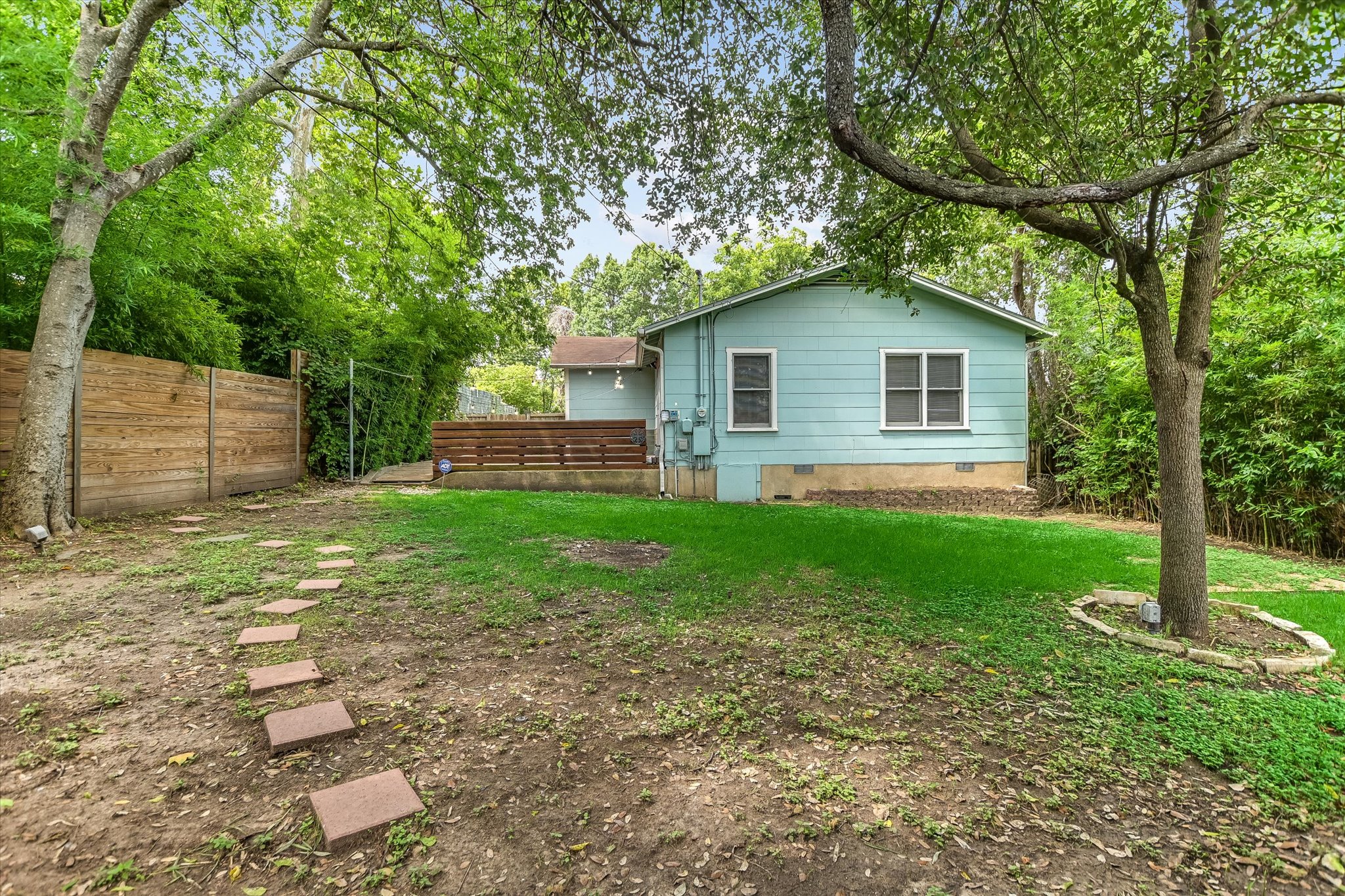 208 Braeswood Road Austin, TX 78704 - Photo 20 of 20 A fenced backyard offers a private retreat with a wooden deck, mature trees, and stepping stones leading across the lawn.