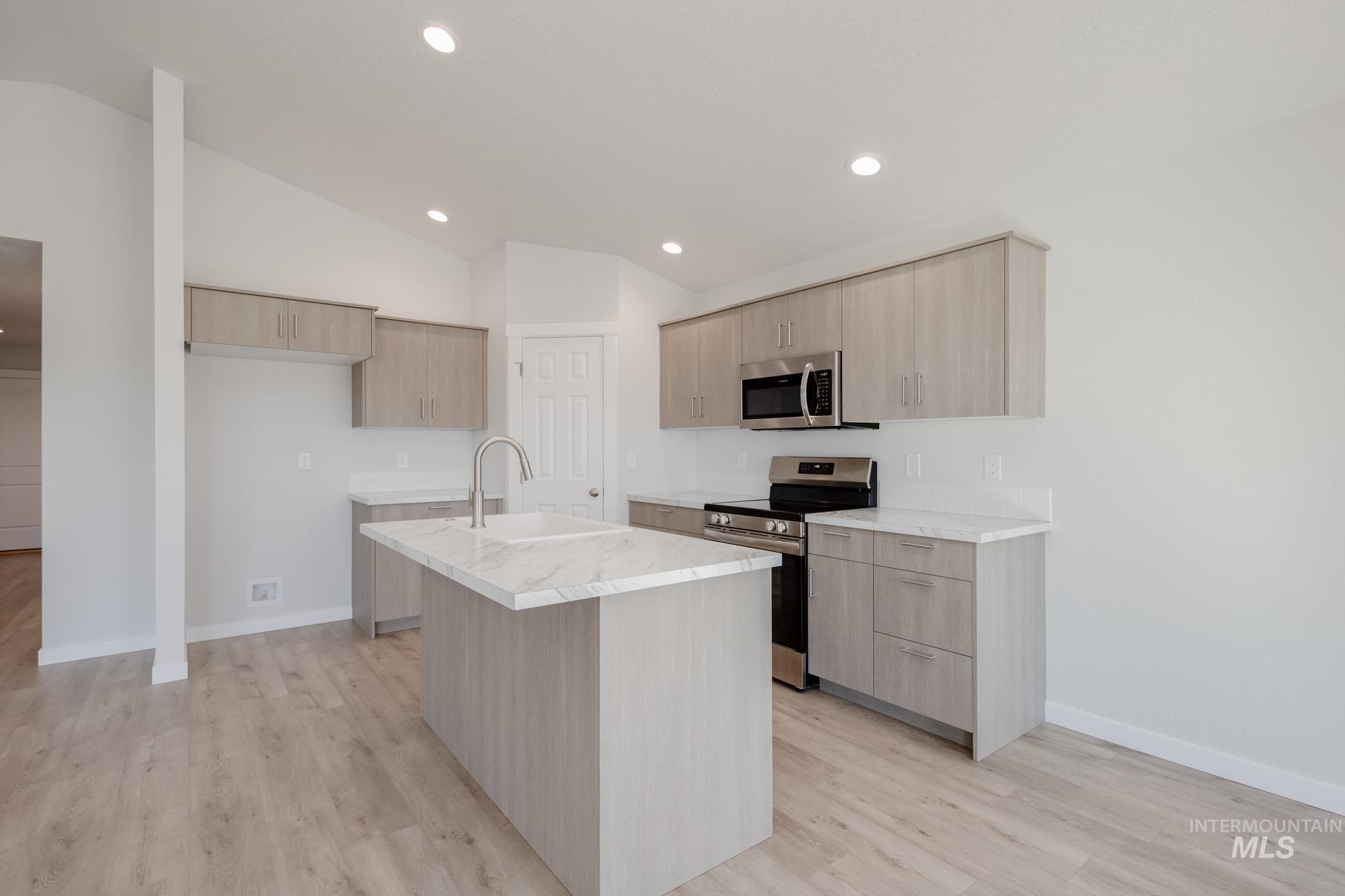 14092 Shiny Spruce Street Caldwell, ID 83607 - Photo 5 of 22 Modern kitchen featuring wood-finish flooring, light-toned cabinetry, stainless steel appliances, a center island with an undermount sink, and recessed lighting