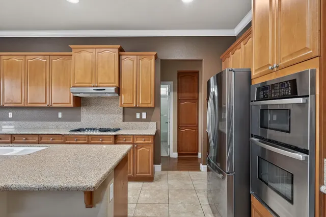 a kitchen with stainless steel appliances granite countertop a refrigerator a stove and a sink with wooden cabinets