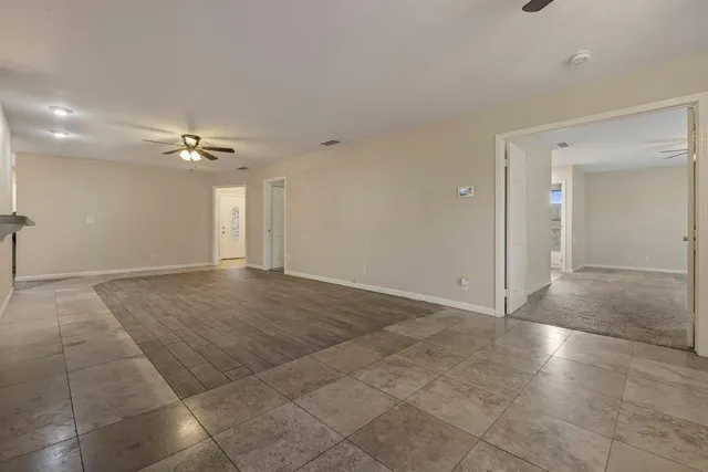 a view of an empty room with chandelier fan and window