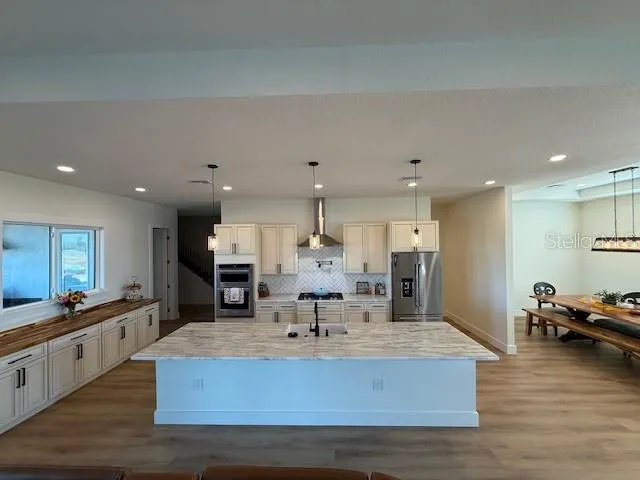 a large living room with stainless steel appliances kitchen island granite countertop a refrigerator a stove a sink dishwasher and a dining table with wooden floor