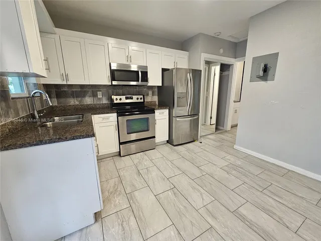 a kitchen with stainless steel appliances granite countertop a refrigerator a stove a sink and white cabinets