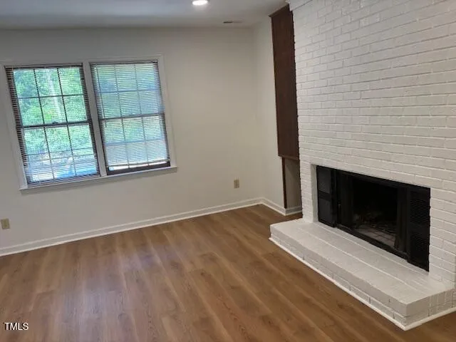 an empty room with wooden floor fireplace and windows