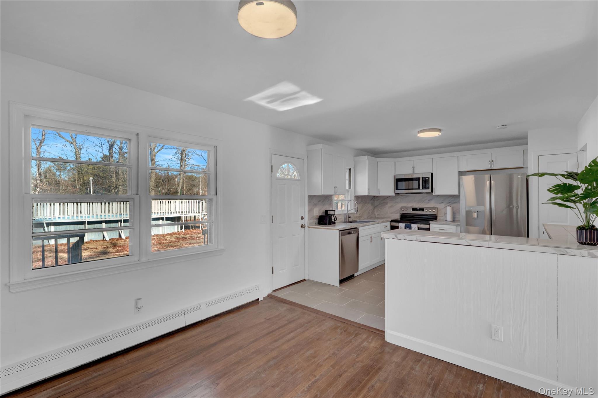 57 Middle Island Road Medford, NY 11763 - Photo 3 of 27 Kitchen featuring baseboard heating, appliances with stainless steel finishes, white cabinets, light wood-style flooring, and decorative backsplash