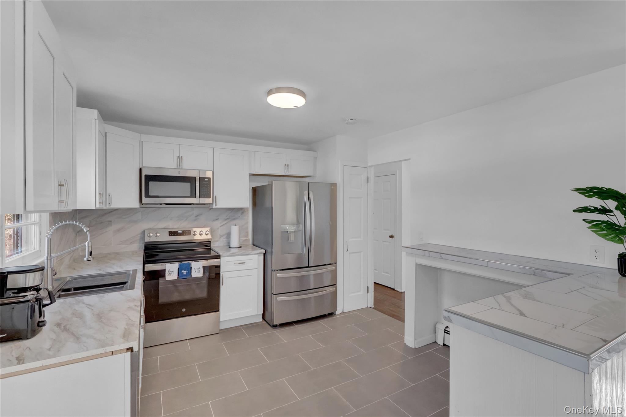 57 Middle Island Road Medford, NY 11763 - Photo 6 of 27 Kitchen featuring stainless steel appliances, light countertops, white cabinetry, and decorative backsplash