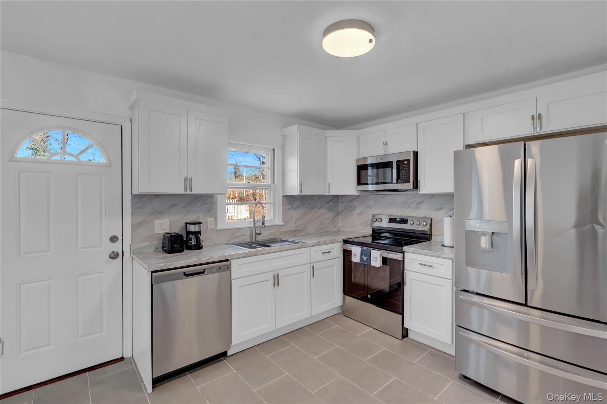 57 Middle Island Road Medford, NY 11763 - Photo 7 of 27 Kitchen with stainless steel appliances, white cabinetry, tasteful backsplash, and light tile patterned flooring