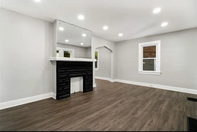 an empty room with wooden floor fireplace and windows