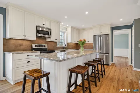 a kitchen with stainless steel appliances granite countertop a stove a sink a refrigerator and white cabinets with wooden floor