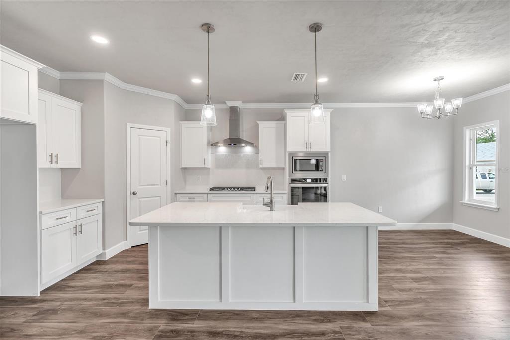 1140 Southwest 67th Street Gainesville, FL 32607 - Photo 25 of 65 a large white kitchen with kitchen island a sink wooden floor and stainless steel appliances