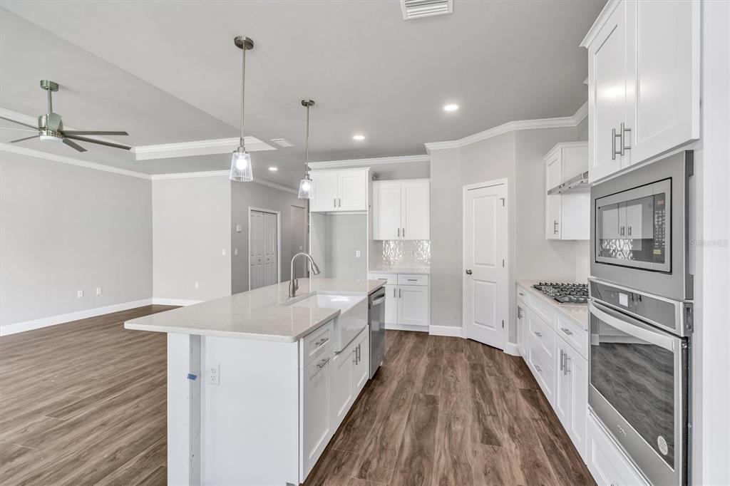 1140 Southwest 67th Street Gainesville, FL 32607 - Photo 28 of 65 a large kitchen with kitchen island a stove a sink dishwasher a refrigerator and white cabinets with wooden floor