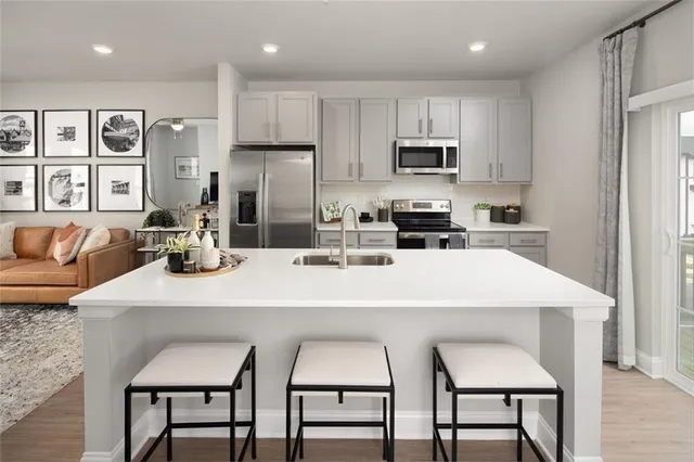 a kitchen with stainless steel appliances granite countertop a stove a sink a microwave a refrigerator and white cabinets with wooden floor