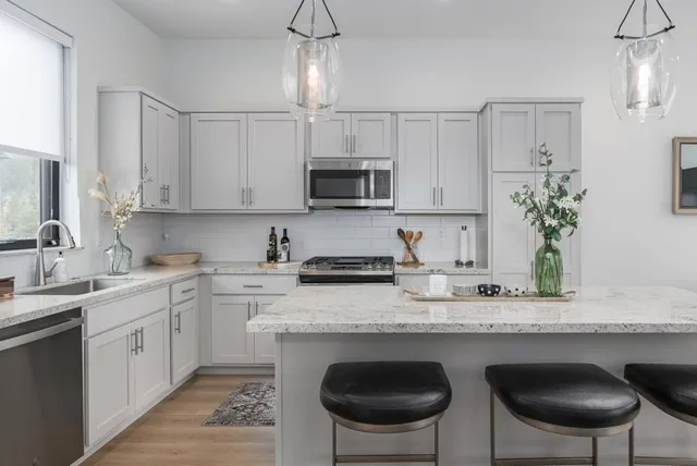 a kitchen with stainless steel appliances granite countertop a stove a sink a microwave a refrigerator and white cabinets