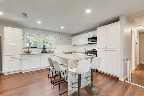a kitchen with stainless steel appliances granite countertop a refrigerator a sink dishwasher a stove a dining table and chairs with wooden floor