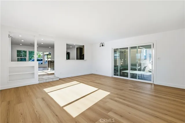 a view of an empty room with wooden floor and a kitchen