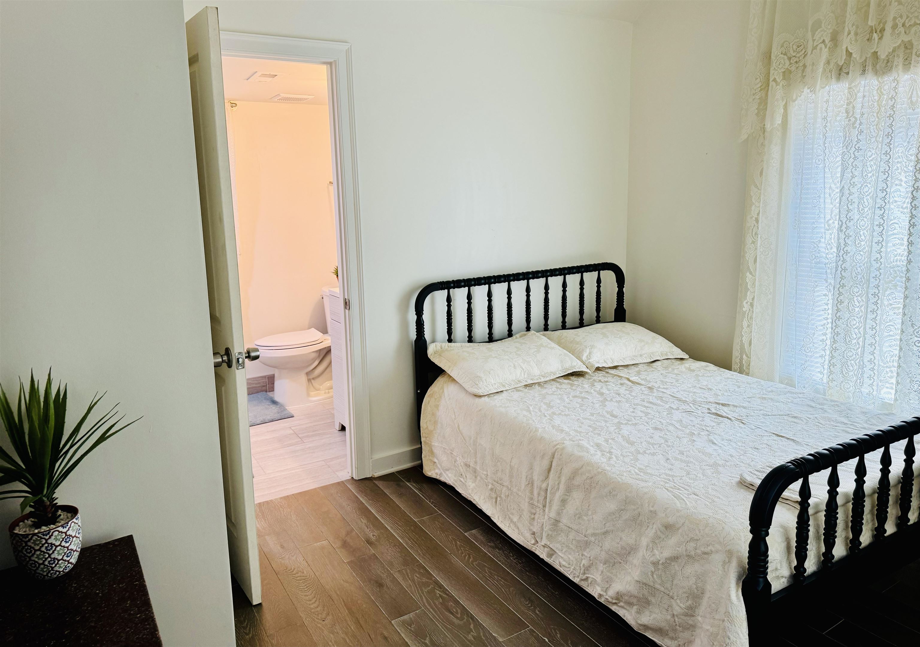 Bedroom with dark wood-type flooring and connected bathroom