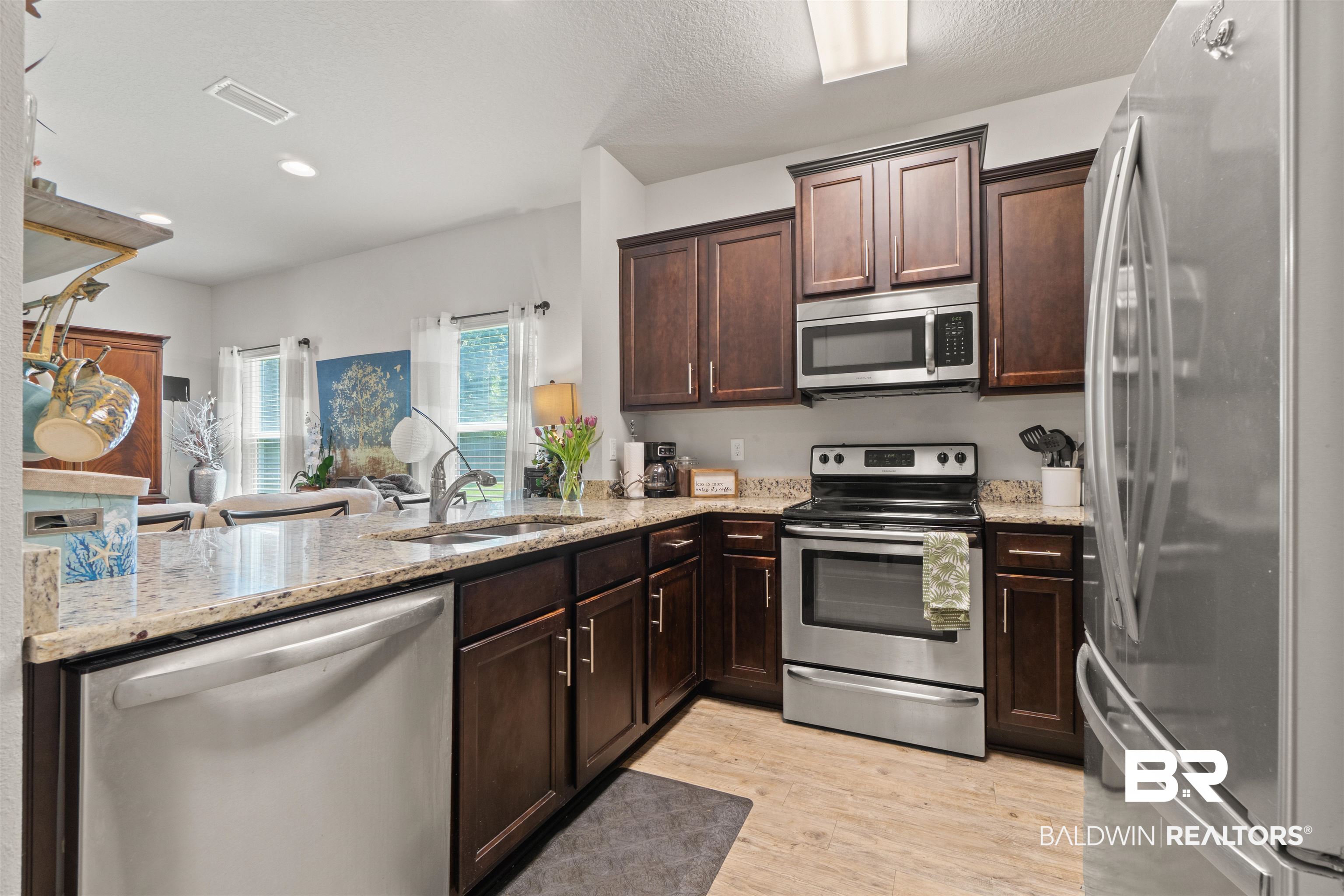 25806 Pollard Road, Unit 6 Daphne, AL 36526 - Photo 8 of 38 Kitchen featuring wood-finish flooring, dark wood cabinetry, light-toned countertops, and stainless steel appliances including a refrigerator, range, microwave, and dishwasher