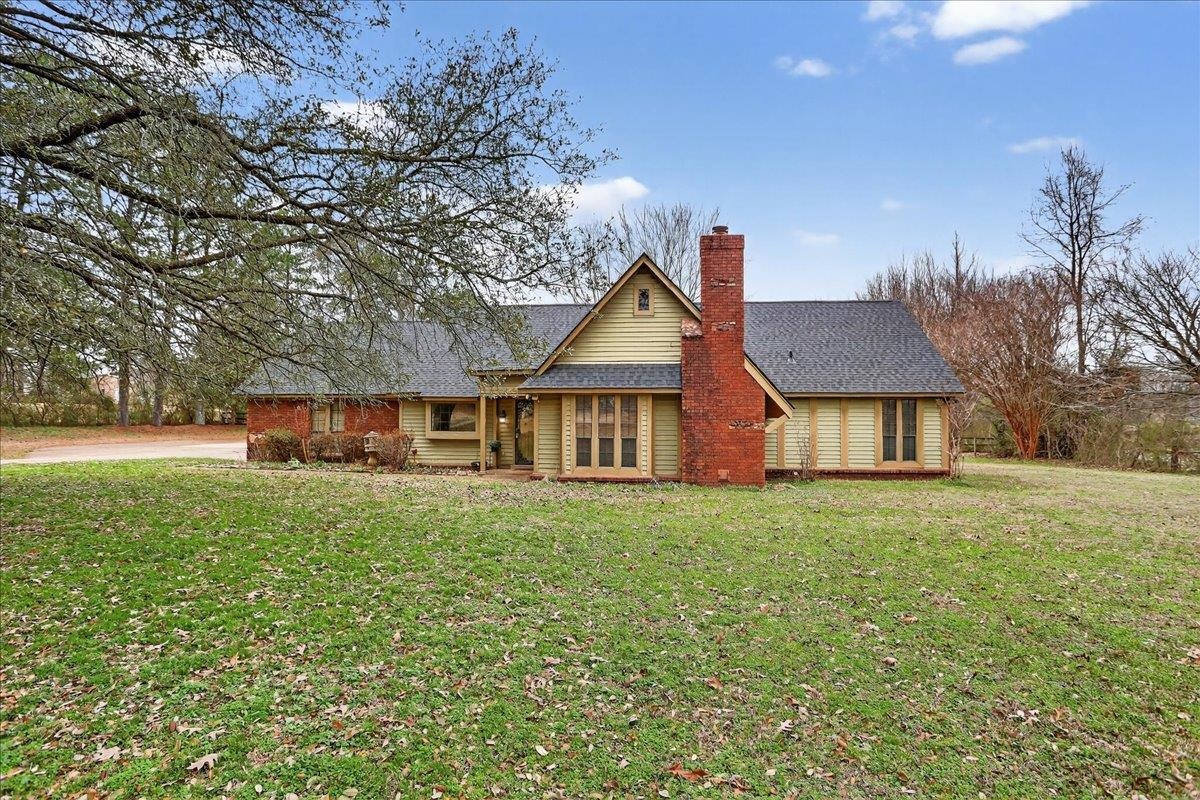 View of front of property featuring a front yard, a chimney, and roof with shingles