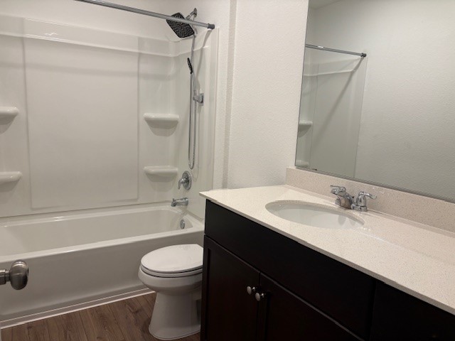 147 Gabbro Gardens Maxwell, TX 78656 - Photo 8 of 14 Bathroom featuring a white tub and shower combination with a rainfall showerhead, a toilet, a dark wood-finish vanity with a light-colored countertop, and a large wall-mounted mirror