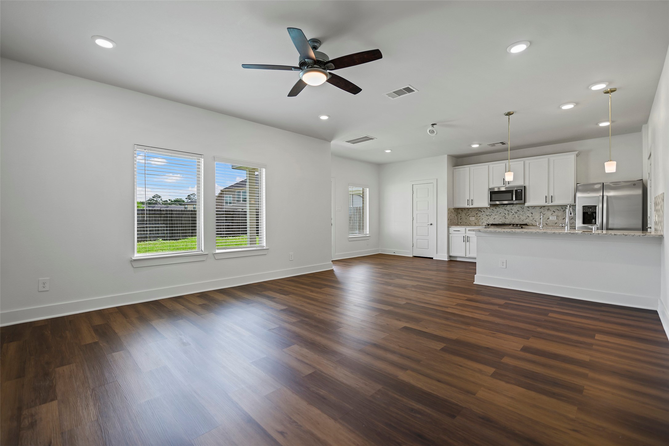 10603 Whitejacket Conroe, TX 77385 - Photo 23 of 42 The living room has a spacious open-concept living area features elegant wood flooring, abundant natural light from large windows, and a modern kitchen with stainless steel appliances, white cabinetry, and granite countertops. A ceiling fan and recessed lighting add comfort and style.